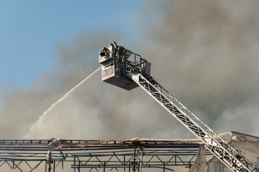 Firefighter on ladder watering roof of building