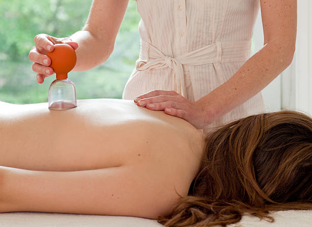 Female patient at the alternative practitioner "A young woman patient is being treated with cupping, an alternative medicine procedure" cupping therapy stock pictures, royalty-free photos & images