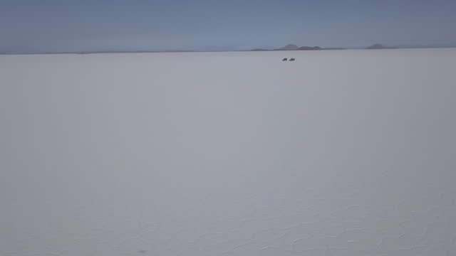 Aerial drone shot of a 4x4 offroad vehicle driving on the Salar de Uyuni salt lake around the isla pescado, fish island, on the biggest salt flat in the world in high altitude of the Andes in the Bolivia.