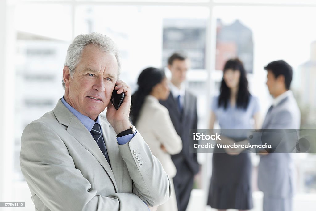 Serious and mature manager talking on the phone Serious and mature manager talking on the phone while his team is behind him 20-29 Years Stock Photo