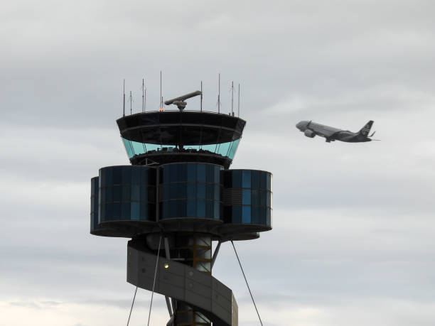 An Air New Zealand Airbus A320-271NX plane, registration ZK-NHB, taking off from the main runway of Sydney Kingsford-Smith Airport as flight NZ226 to Christchurch.  In the foreground is the air traffic control tower. The silhouette of an air traffic control operator is visible in the tower. This image was taken from off Ross Smith Avenue, Mascot on an overcast and rainy afternoon on 4 November 2023.