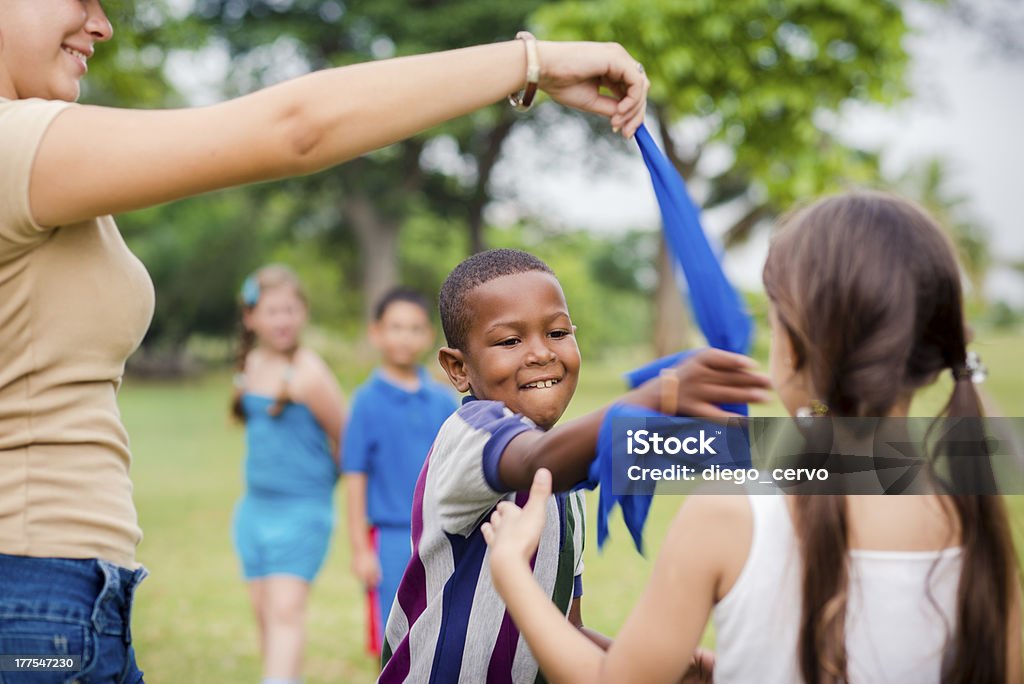 Children and teacher playing games in city park "People and fun, group of male and female school kids with young woman working as educator playing game outdoor at summer camp" Summer Camp Stock Photo