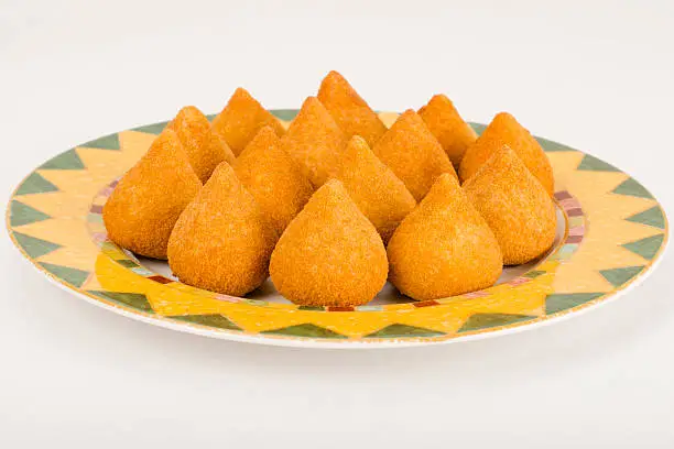 Coxinha de Galinha - Brazilian breaded and deep fried snacks filled with shredded chicken on a colourful plate on a white background.