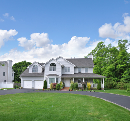 Beautiful landscaped suburban home with blacktop circular driveway blue sky day with clouds