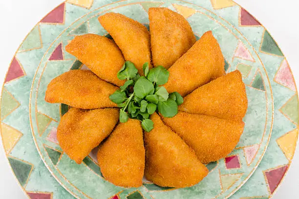 Rissole - breaded and deep fried snacks filled with shredded chicken on a colourful plate on a white background.