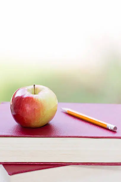Photo of Red & green apple on stack of books with pencil