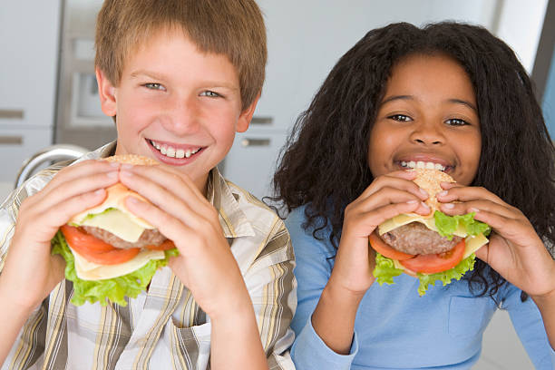 istock Two young children in kitchen eating cheeseburgers smiling 177550820