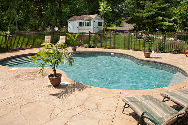 Lush backyard swimming pool and patio space. "Lush, resort-like backyard salt water swimming pool with flagstone stamped concrete patio.  Bronze fencing is seen around pool area." outdoor shed stock pictures, royalty-free photos & images