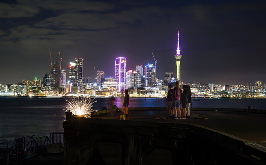 Sky Tower lit up in pink and yellow to celebrate Diwali. Family and friends lighting fireworks for Guy Fawkes. Auckland.