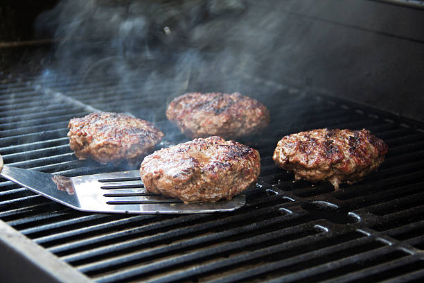 Hamburgers on the grill Four hamburgers cooking on a barbeque grill, one in the process of being turned over by a spatula. grill burgers stock pictures, royalty-free photos & images