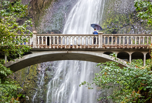 Bridge in front  of giant waterfall in Oregon. Person with umbrella on the bridges