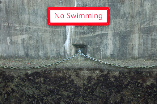 No Swimming sign on a damp concrete canal wall with no visible water