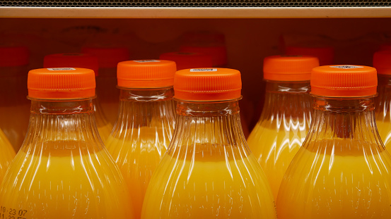 Many beautiful bottles of orange juice on the shelf of a fridge close-up