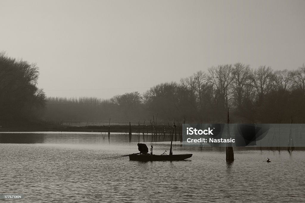 Fishing at Sunset A man fishing from a small boat as the sun sets over a lake. Aquatic Sport Stock Photo