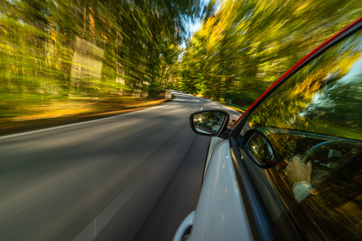 driving on country road through autumn colored forest on sunny day, dynamic car image with motion blure