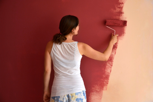 Beautiful young woman in causal clothes painting a wall with red paint and a roller