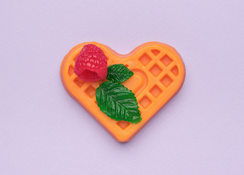 Raspberries, two leaves and a cookie figurine on a purple background. Creative dessert.