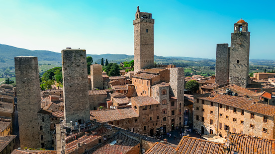 Aerial view of the town of San Gimignano in Tuscany Italy with summer weather, Aerial view of the town of San Gimignano in Tuscany, one of the most beautiful medieval towns in the Tuscany region of Italy\n\nSan Gimignano is a small walled medieval hill town in the province of Siena, Tuscany, north-central Italy. Known as the Town of Fine Towers, San Gimignano is famous for its medieval architecture, unique in the preservation of about a dozen of its tower houses.\n\nThe Palazzo Comunale, the Collegiate Church and Church of Sant' Agostino contain frescos, including cycles dating from the 14th and 15th centuries. The \