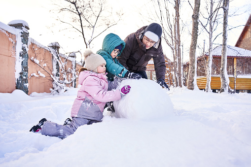 A family builds a snowman out of snow in the yard in winter.