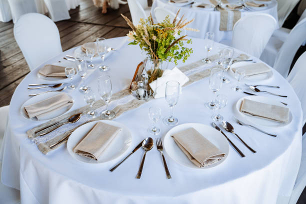 istock Serving a festive table, placing plates on the table, a Banquet table with a white tablecloth, preparing the dining table for the holiday, Cutlery is arranged according to etiquette. flowers on the table. 1775788238