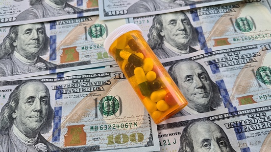 Pills and capsules in a bottle on US dollars bills. Concept of health care in USA, pharmaceutical business