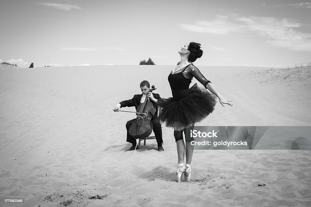 Cultural encounter in the desert A solo cellist plays for an elegant ballerina dancing in the barren desert. Dancing Stock Photo