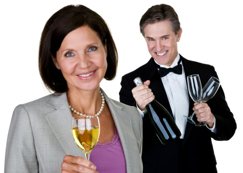 Closeup of a beautiful mature woman holding a glass of champaign and a handsome man in the background wearing a tuxedo 