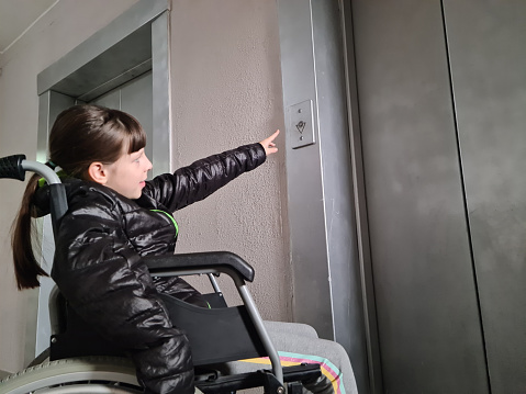 Disabled teenage girl in wheelchair who decides to use elevator on own. Lifestyle of child with special needs at educational age