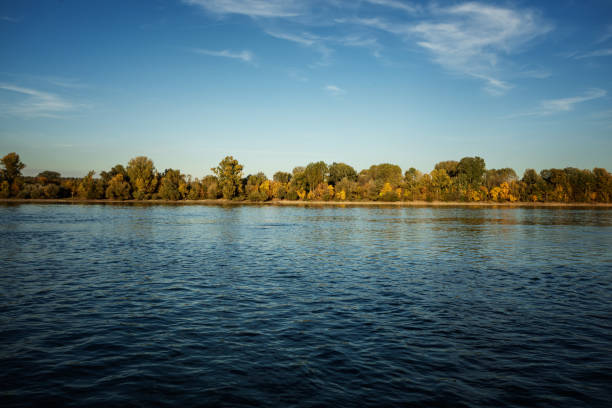 Autumn scene from river, river shore reflecting at blue water surface at sunny autumn day, late afternoon, no people