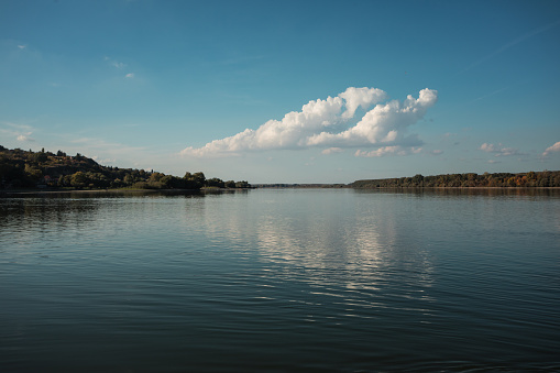 Autumn scene from river, river shore reflecting at blue water surface at sunny autumn day, late afternoon, no people