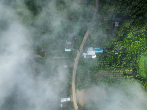 Aerial top view flying over mountains and rural villages in mist-shrouded morning.