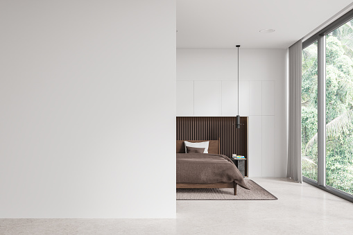 Interior of stylish bedroom with white walls, concrete floor, comfortable king size bed with brown blanket, cozy round bedside table and copy space wall on the left. 3d rendering