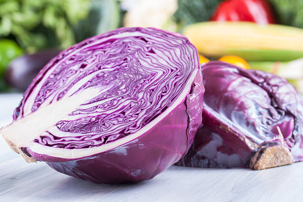 A red cabbage sliced in half in front of vegetables Close up photo of edible vegetables - a red cabbage with some vegetables in the background on a solid light blue wooden table red cabbage stock pictures, royalty-free photos & images