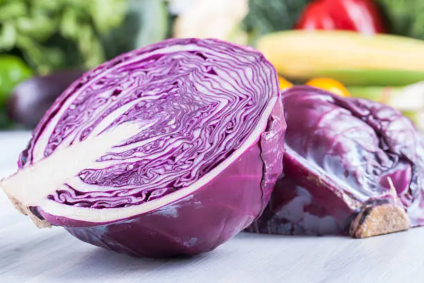 Close up photo of edible vegetables - a red cabbage with some vegetables in the background on a solid light blue wooden table