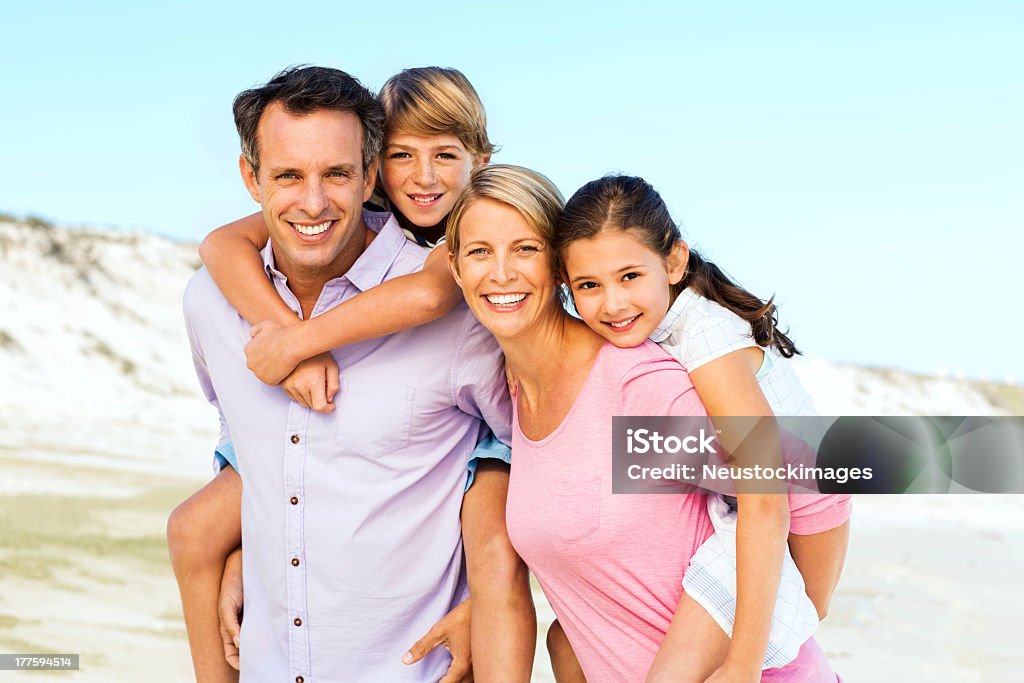 Parents Piggybacking Children At Beach Portrait of happy parents piggybacking children against clear blue sky on beach. Horizontal shot. 10-11 Years Stock Photo