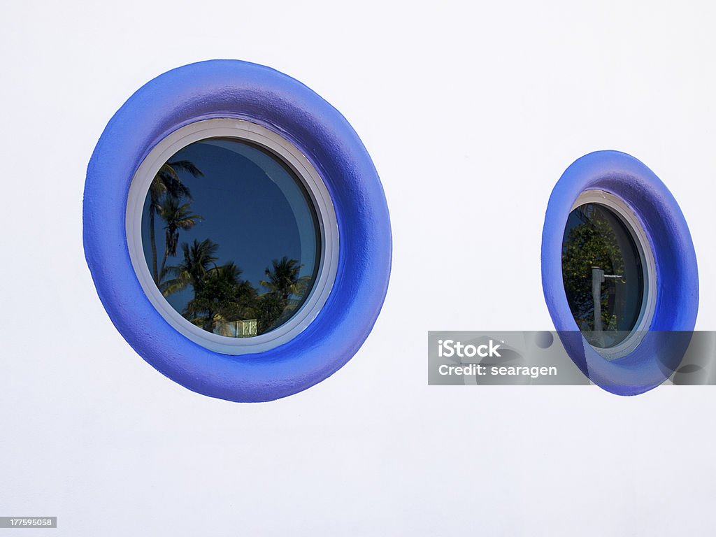 Two Round Art Deco Windows Two round windows painted in deep blue anchor an exterior wall on a building in South Beach in Miami. The reflection in the window shows the palm trees near the beach. Art Deco Stock Photo