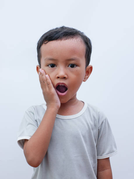 porträt eines kleinen asiatischen jungen, der sich mit zahnschmerzen die wange h�ält. unter zahnschmerzen schmerzen im mund - human teeth little boys behavior expressing negativity stock-fotos und bilder