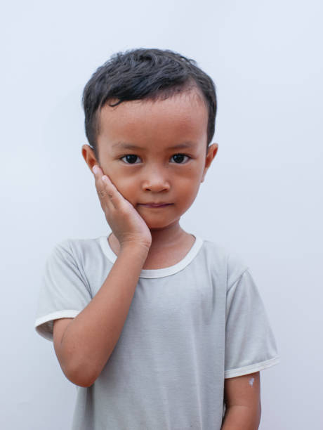 porträt eines kleinen asiatischen jungen, der sich mit zahnschmerzen die wange hält. unter zahnschmerzen schmerzen im mund - human teeth little boys behavior expressing negativity stock-fotos und bilder