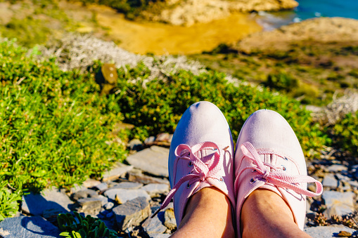 Female feet in sneakers against mediterranean sea coast landscape. Murcia region, Calblanque Park in Spain. Hiking, vacation activity.