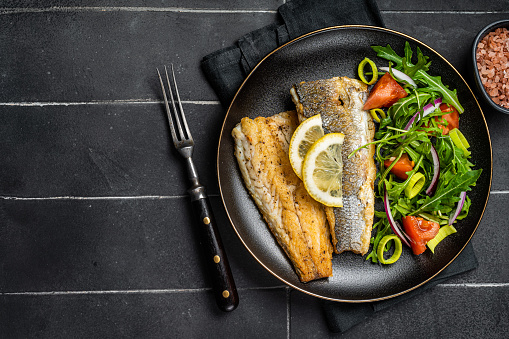 Roasted sea bass fillet with salad, Branzino fish. Black background. Top view. Copy space.
