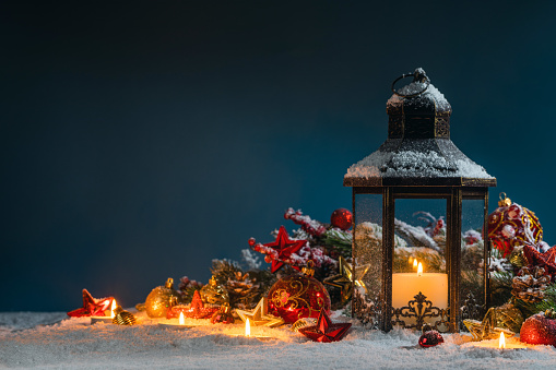 Glowing Christmas lantern and decor of fir tree branches and baubles in snow