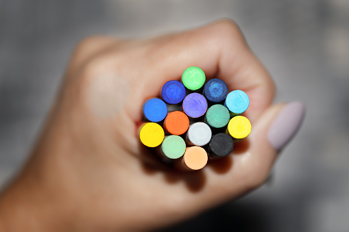 Colored chalks clamped to a fist on a gray background. Shallow depth of field