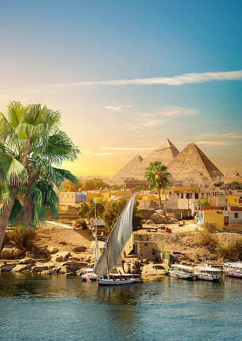 River Nile and boats at sunset in Aswan and pyramids