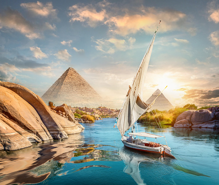 River Nile and boats at sunset in Aswan and pyramids