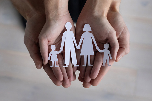 family with children concept, family insurance, hands holding married paper couple with two kids