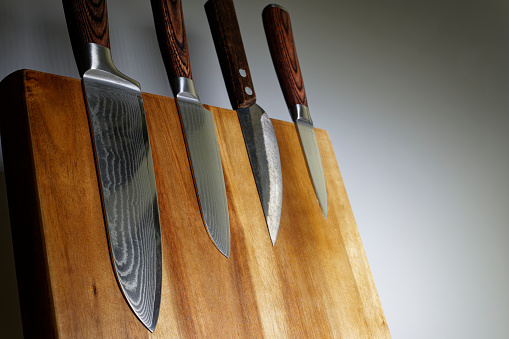 Japanese knives with blades made of beautifully textured Damascus steel on a wooden knife block.