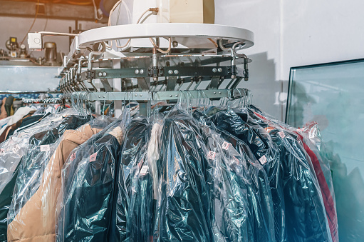 Front view of clothes on hangers in dry cleaners. Conveyor with hangers of cleaned items