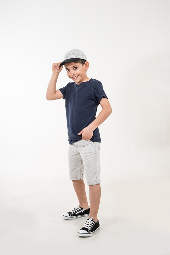 boy is on white background he is touching his right hand to grey hat vertical still