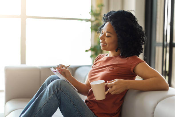 istock Happy black lady relaxing at home, drinking coffee and writing in notepad 1776137541