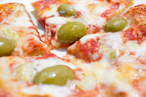 Visione parziale di una pizza Margherita con olive verdi, divisa in spicchi.